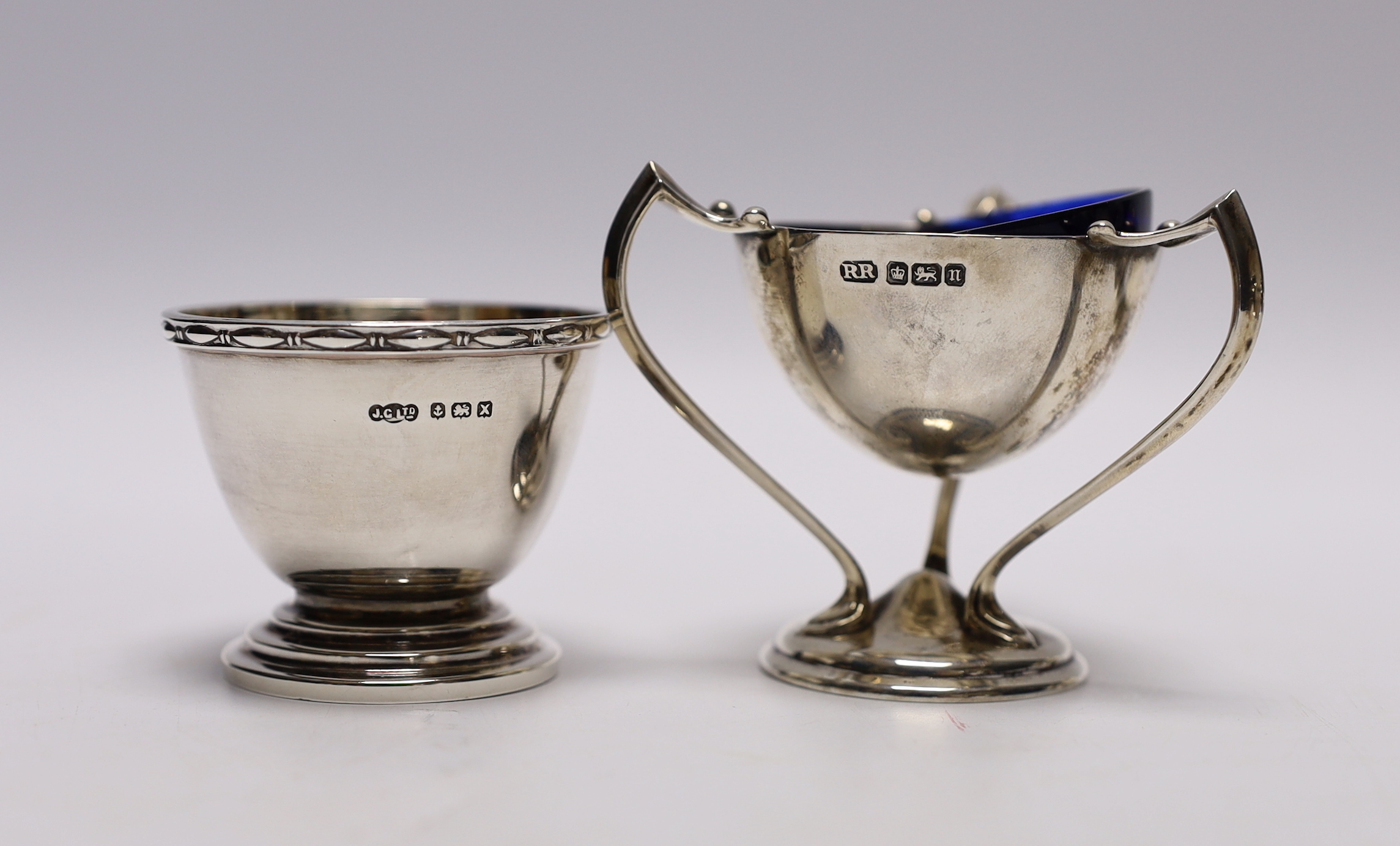 A pair of Edwardian Art Nouveau silver tri-handled salts, Richard Richardson, Sheffield, 1905, height 59mm, together with a later silver three piece condiment set, with two spoons (one plated).